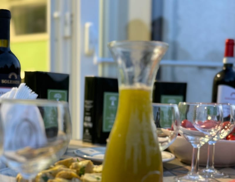 Ein gedeckter Tisch am Abend: Karaffe mit frisch gepresstem Öl, Fogliantica-Geschenkboxen und Wein